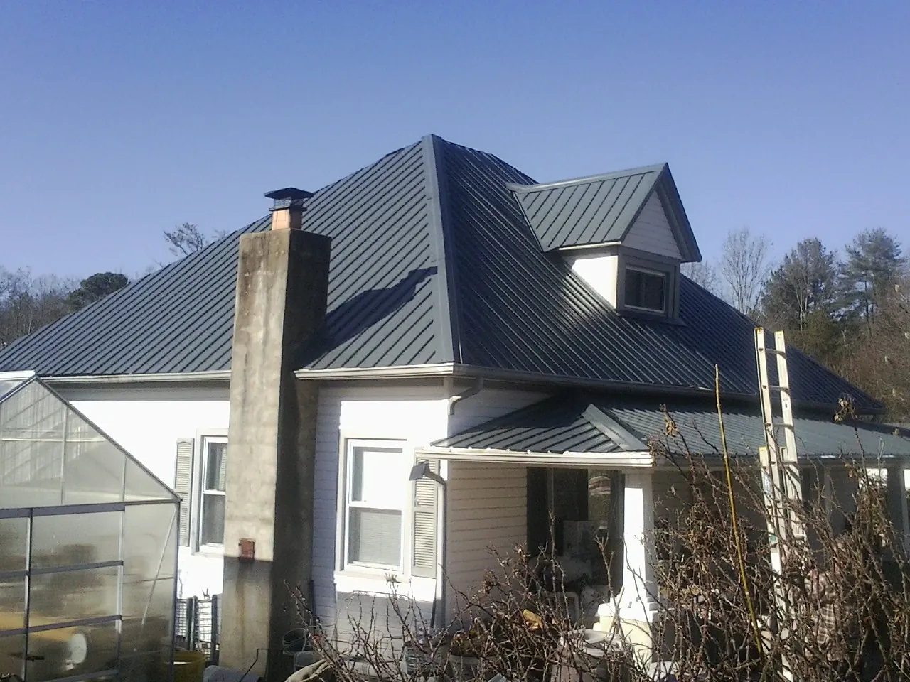 Dark blue standing seam metal roof on a white farmhouse with dormer — Slate & Tile Roof Repair by Roofing Brothers in Mallory