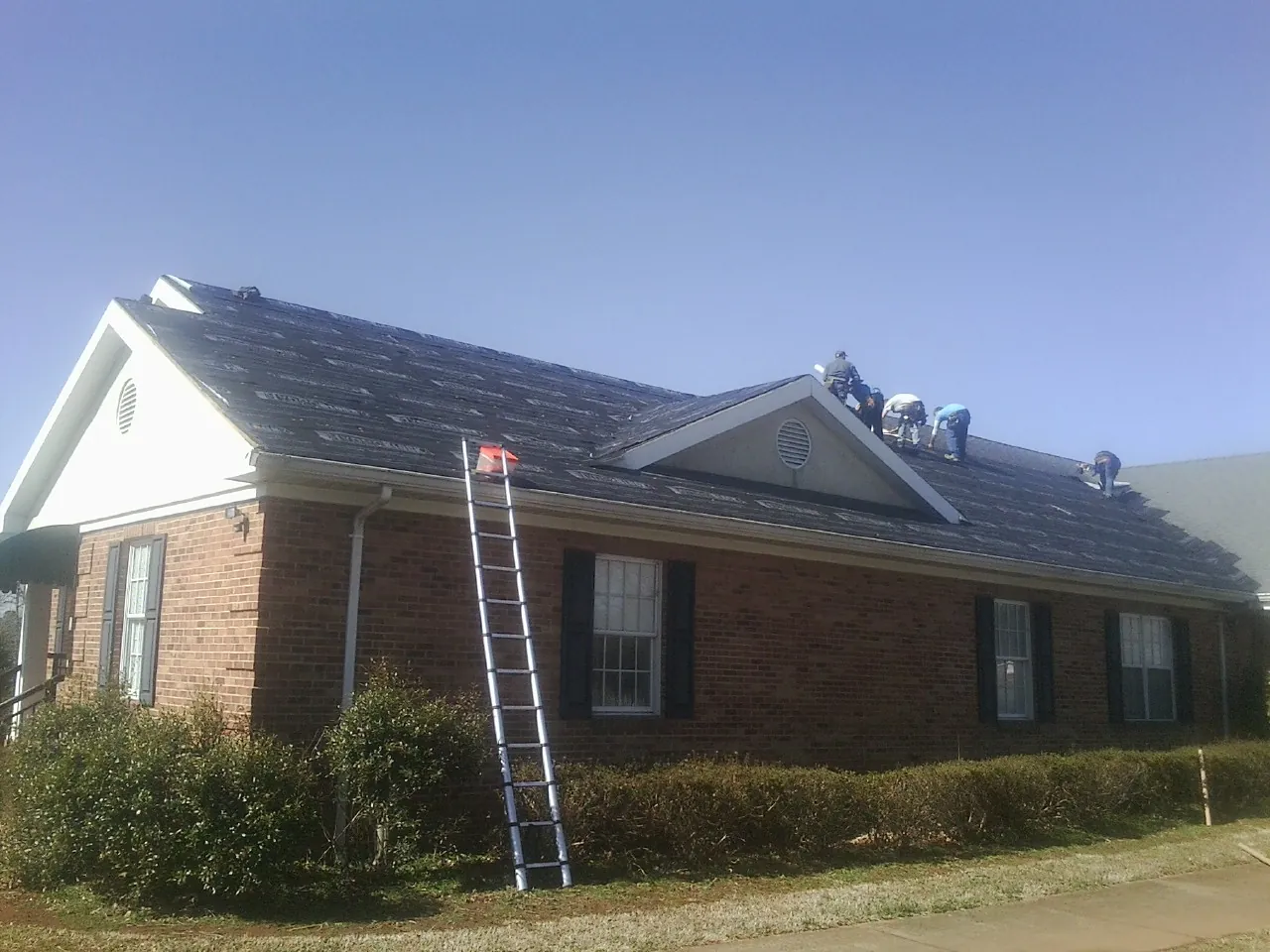 Crew tearing shingles off a brick ranch roof with a ladder set — Emergency Roof Repair work by our crew in Mallory