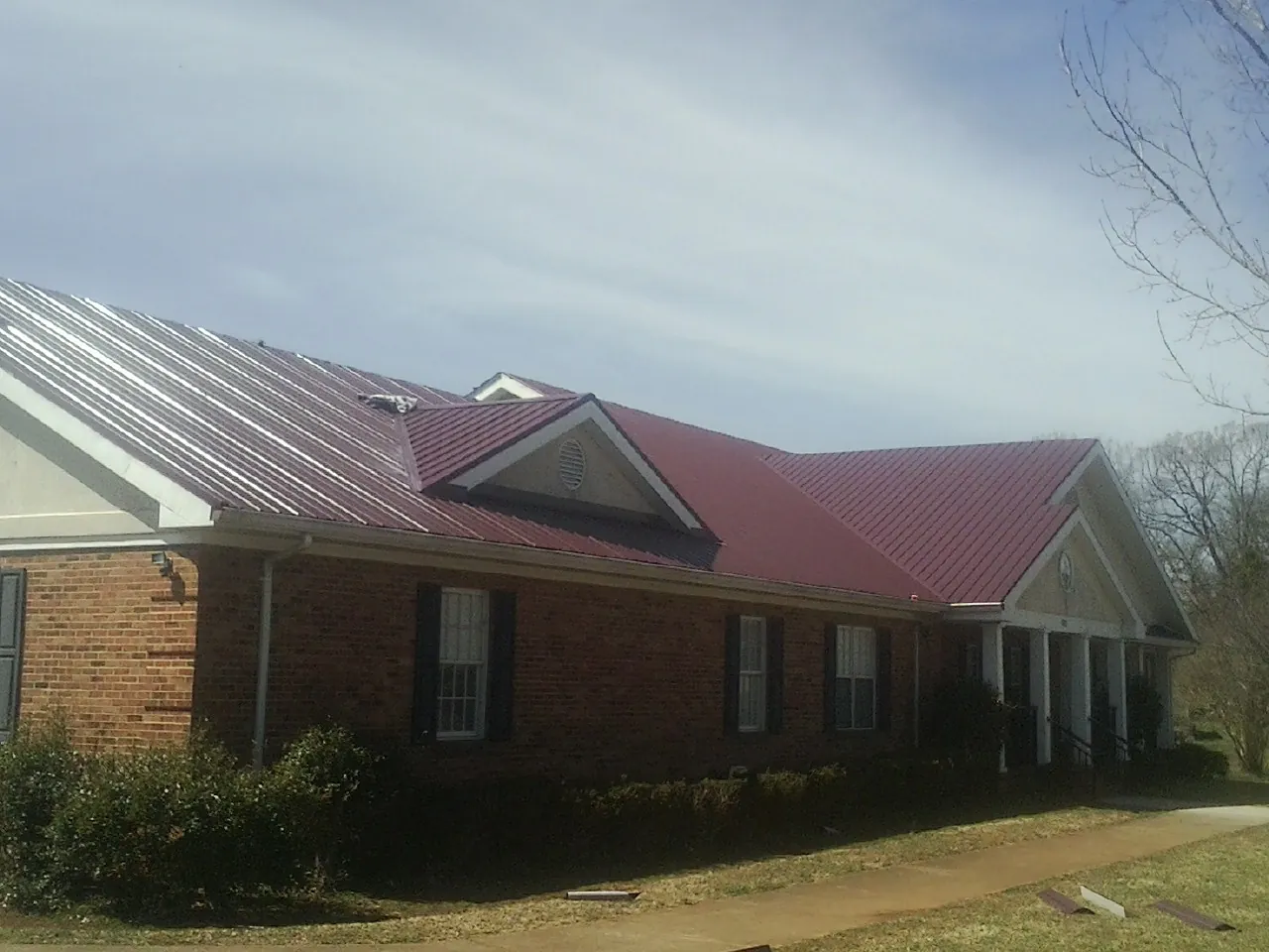 Red metal roof with gabled entries on a long brick building, from a Hail Damage Roof Repair job in Mallory