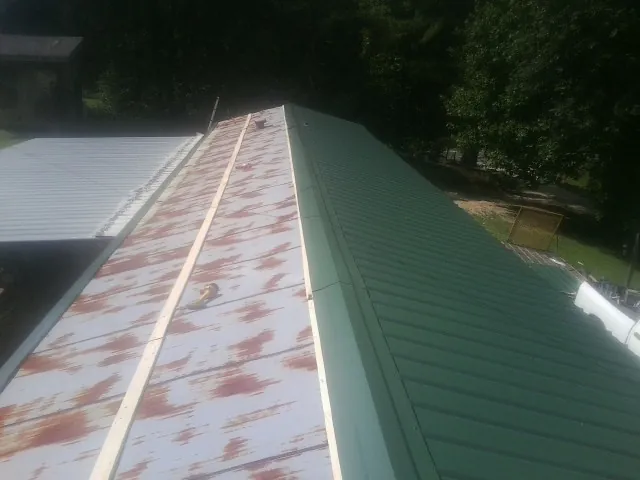 Old rusted panels beside newly installed green metal roofing — Wind Damage Roof Repair by Roofing Brothers in Mallory