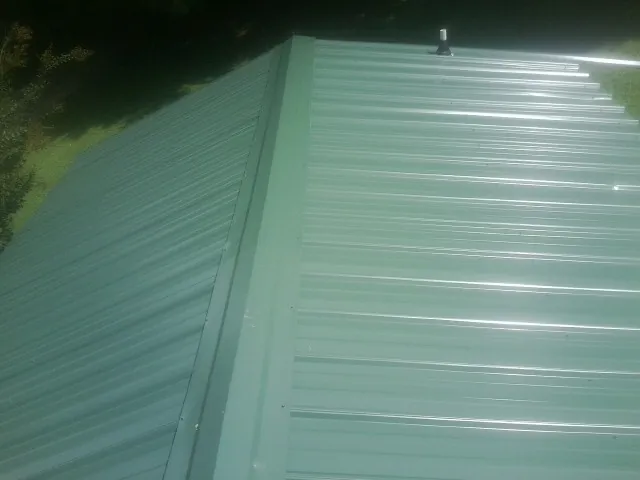 New green metal panels meeting at the ridge of a roof — Flat Roof Repair work by our crew in Mallory
