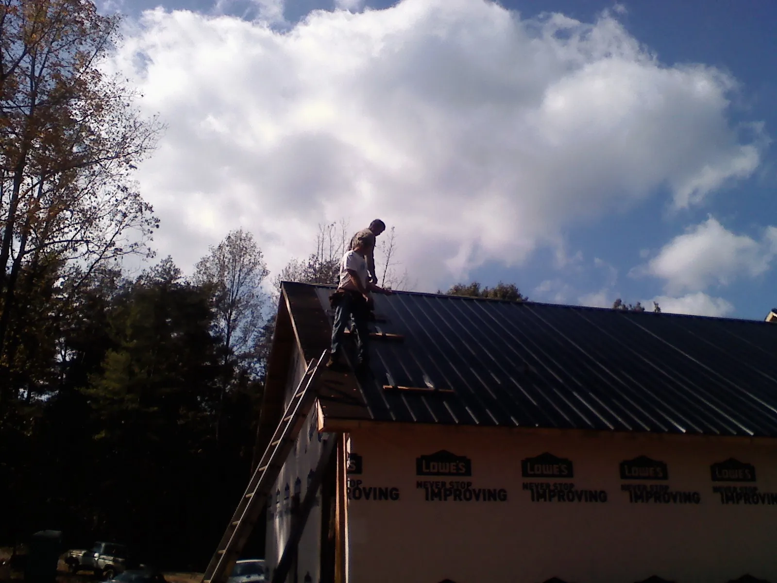 Roofer fastening dark metal panels high against a cloudy sky, from a Roof Inspection job in Mallory