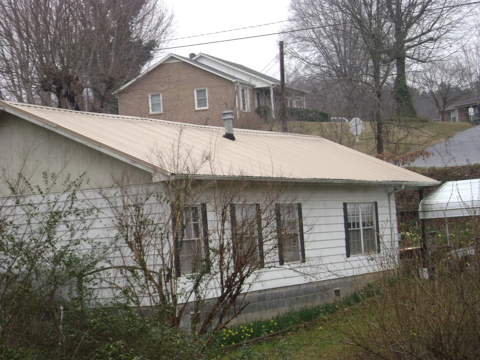 Tan metal roof on a white sided house set into a hillside — Commercial Roofing by Roofing Brothers in Mallory